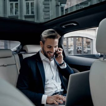 Handsome young man in full suit talking on smart phone and smiling while sitting in the car